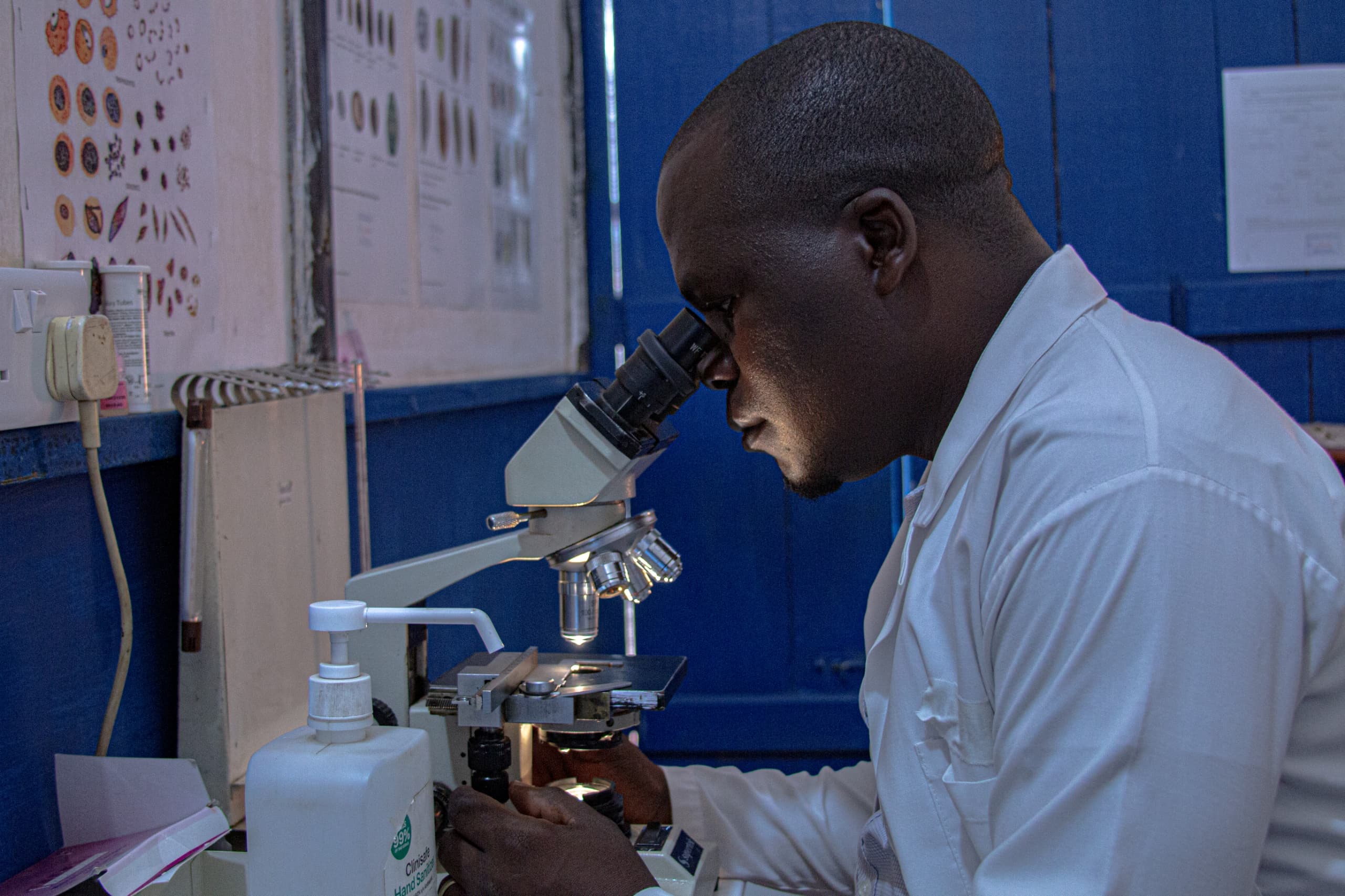 A Mysha lab technician in a white coat examining a slide under the microscope